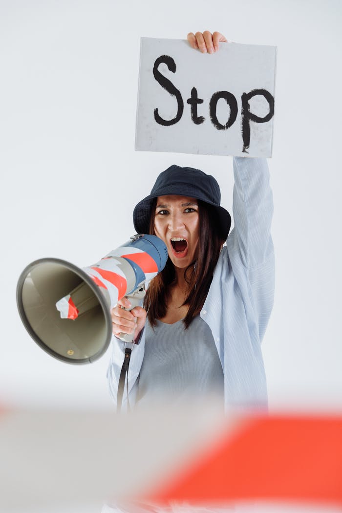 Young woman in a studio holding a stop sign and megaphone, expressing protest and activism.